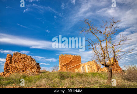 Une photo en mode paysage avec un seul arbre mort et les ruines d'une vieille maison de ferme au milieu d'une zone herbeuse à sec avec un ciel bleu et les nuages blancs au-dessus Banque D'Images