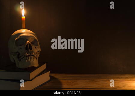 Crâne humain avec la lumière des bougies et le livre sur la table en bois dans l'arrière-plan sombre, décorer pour Halloween Theme avec copie espace. Banque D'Images
