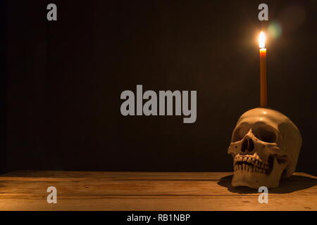 Crâne humain avec la lumière des bougies sur table en bois dans l'arrière-plan sombre, décorer pour Halloween Theme avec copie espace. Banque D'Images