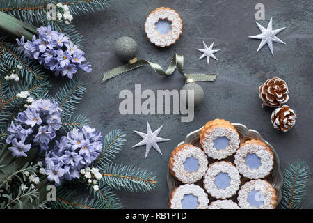 Vue de dessus avec les cookies Linzer fleurs vitrage bleu foncé sur fond d'hiver en vert sapin décoré avec des brindilles, des fleurs de jacinthe bleu, pommes de pin et Banque D'Images