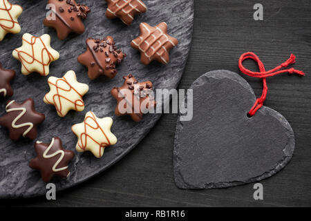 Chocolats en forme d'étoile sur le conseil de pierre gris foncé avec cœur noir sur fond texturé noir Banque D'Images