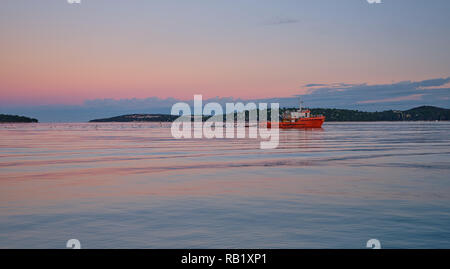 Bateau de pêche orange à revenir au port tôt le matin d'être suivre par un troupeau de mouettes. Sky a de belles teintes de rose brune orangé Banque D'Images