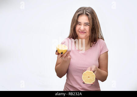 Jeune femme se rétrécit de citron aigre. Elle tenir dans les mains. agrumes jaune Isolé sur fond gris. Banque D'Images