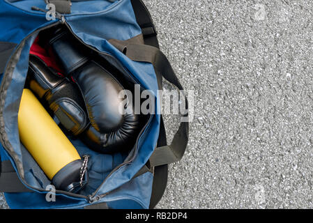 La préparation au combat. Close-up de sac de sport et des gants de boxe avec de l'eau à l'arrière-plan d'asphalte Banque D'Images