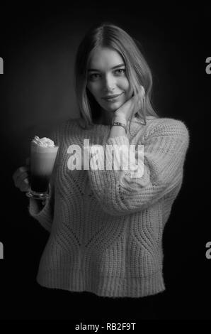 Jolie jeune femme avec un café irlandais. Belle blonde dans un chandail avec une grande tasse de café avec de la crème. Banque D'Images