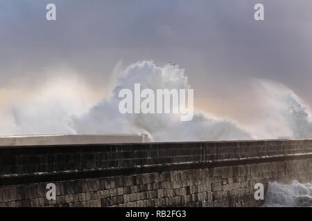 De fortes vagues se briser contre pier avec intéressant fin de journée lumière filtre à travers les nuages et l'humidité. Porto, Portugal, en janvier. Banque D'Images