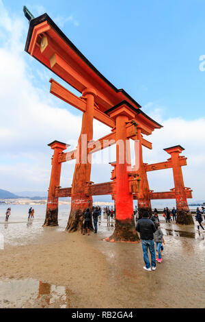 Le Japon. Le Grand Torii au sanctuaire Shinto d'Itsukushima sur l'île de Miyajima à marée basse avec une foule de gens autour de sa base de six piliers. Banque D'Images