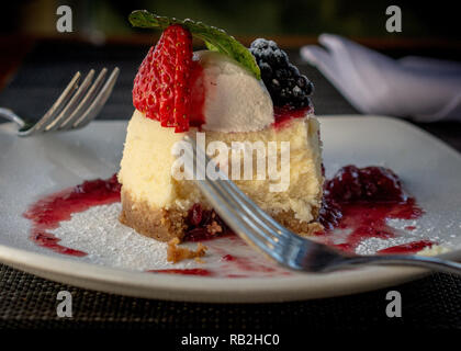Mini cheesecake ronde décorée de fraises et framboises, en partie mangé, et de deux fourches, suggérant un dessert partagé Banque D'Images