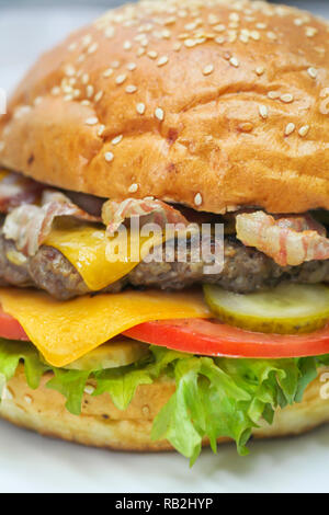 Close up of burger fraîchement préparé avec du boeuf haché et du bacon, fromage cheddar, laitue, concombres et tomates Banque D'Images