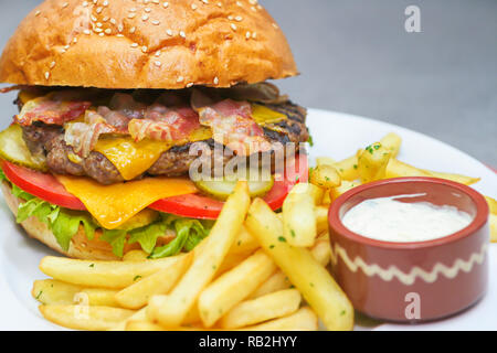 Burger fraîchement préparé avec du boeuf haché et du bacon, du fromage cheddar et frits avec des frites Banque D'Images