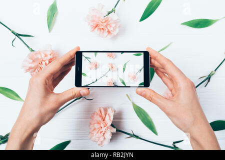 Woman's hands holding faisant photo et smart phone plus décoratif de téléviseur jeter composition florale, photo s'affiche sur l'écran de l'appareil mobile. Banque D'Images