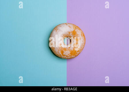 En poudre sucre donut rond sur un fond bicolore, bleu et magenta. Voir ci-dessus dans un style minimaliste avec copie espace Banque D'Images