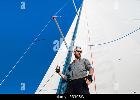 Jeune homme européen debout à bord de yacht à la recherche en mer. Voyageant sur vieux bateau à voile. Style de vie de luxe. Banque D'Images