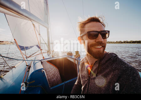 Low angle shot d'un jeune homme portant des lunettes et des gants de marin sur un bateau à voile au coucher du soleil. Les tons de l'image dans des couleurs chaudes. Banque D'Images