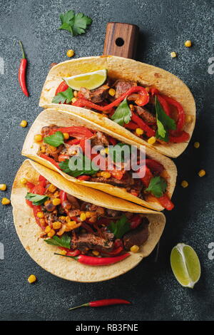 Tacos mexicains au boeuf, légumes et salsa. Les tacos al pastor sur planche de bois sur fond noir. Vue d'en haut. Banque D'Images