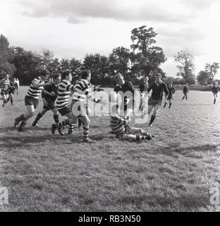 1965, historiques, match de rugby amateur, England, UK, sur une hauteur d'herbe un joueur avec un ballon de rugby s'attaquer par un joueur de l'opposition. Banque D'Images