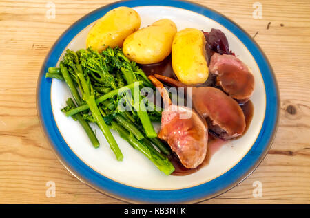 Repas Déjeuner Dîner anglais côtelettes des pommes de terre à la sauce vin rouge brocoli tenderstem et sauce aux canneberges bord bleu plaque blanche sur une table en bois Banque D'Images