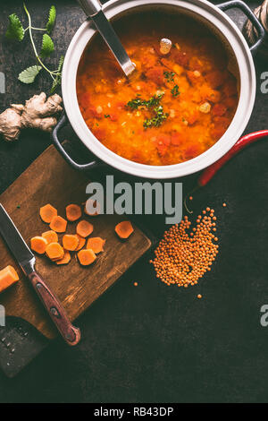 Casserole avec de savoureux soupe de lentilles et louche sur arrière-plan foncé table de cuisine rustique avec des ingrédients, vue du dessus avec l'exemplaire de l'espace. La nourriture végétalienne saine co Banque D'Images