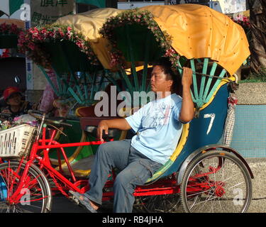 KAOHSIUNG, TAIWAN -- 22 DÉCEMBRE 2018 : un pilote pour un cycle traditionnel rickshaw repose dans le soleil de l'après-midi lors de l'attente pour les passagers. Banque D'Images