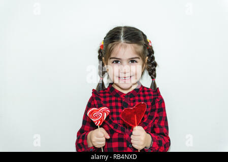 Jolie petite fille adorable lollipop détient dans forme du cœur red candy.Maison de vacances concept avec fond isolé. Banque D'Images