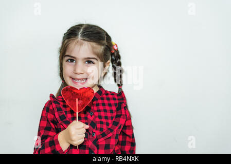 Jolie petite fille adorable lollipop détient dans forme du cœur red candy.Maison de vacances concept avec fond isolé. Banque D'Images