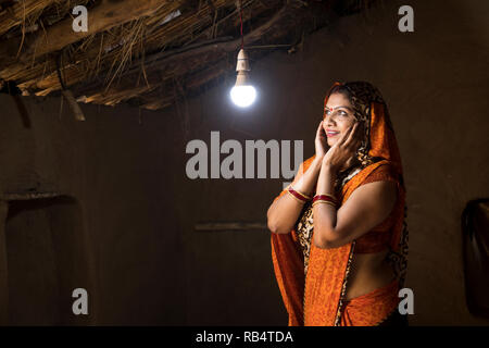 Femme de l'Inde rurale enchanté à la lueur de l'ampoule électrique et de l'électricité à son domicile après une longue attente Banque D'Images