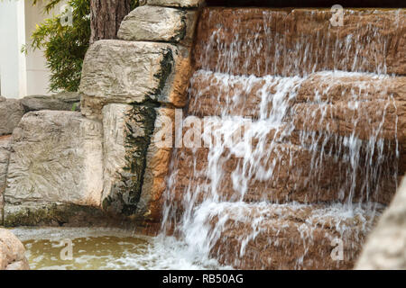 Cool l'eau claire s'écoule à travers une cascade de cascade artificielle faite de pierres. Verse de l'eau ci-dessus et formes mousses lors de tomber vers le bas Banque D'Images