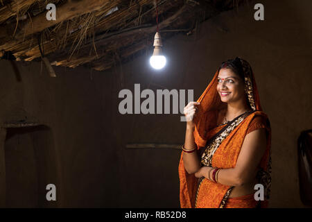 Femme de l'Inde rurale enchanté à la lueur de l'ampoule électrique et de l'électricité à son domicile après une longue attente Banque D'Images