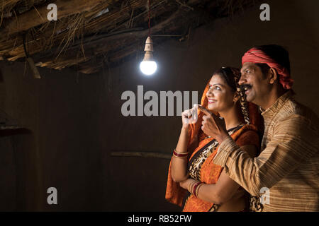 Couple Indien Rural enchanté à la lueur de l'ampoule électrique et de l'électricité d'atteindre leur maison après une longue attente Banque D'Images