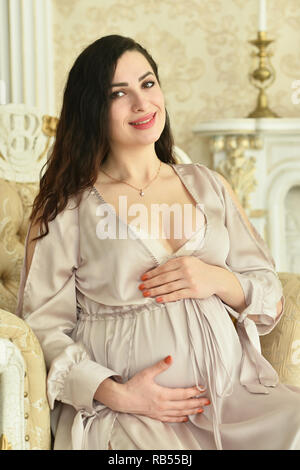 Belle femme enceinte assise sur un fauteuil et posing Banque D'Images