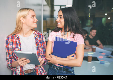 Photo de jeunes modèles blonde and brunette se tenir ensemble et sourire. Ils ont l'air heureux. Les jeunes femmes sont en plastique et électronique comprimés dans les mains. Deux jeunes hommes travaillent derrière eux. Banque D'Images