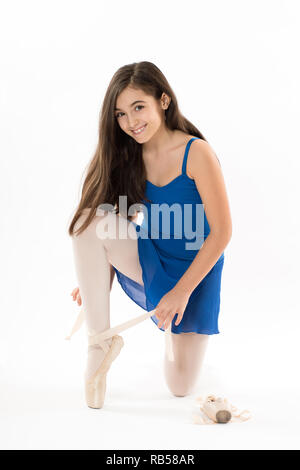 Assez heureux jeune ballerine lier son ballet sur pointes chaussures en tant qu'elle s'agenouille sur le plancher à la recherche à l'appareil photo avec un sourire amical isolated on white Banque D'Images