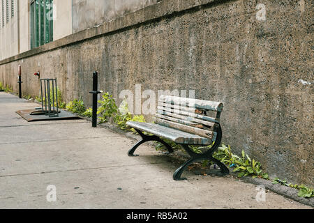 Vieux banc en bois obsolètes sur le trottoir en face d'un mur en béton Banque D'Images