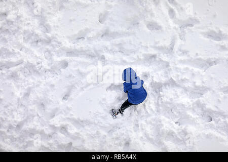 Vue aérienne au-dessus d'un petit garçon face à l' arrière avec manteau bleu jouer dans la neige Banque D'Images