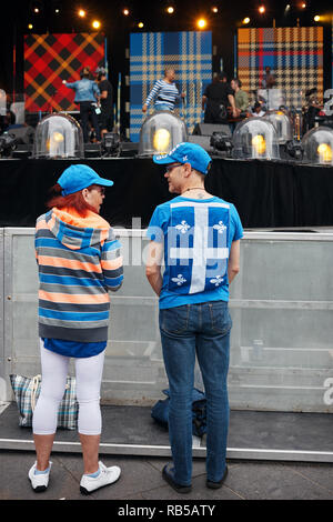 Un jeune homme portant un drapeau du Québec sur son dos en conversation avec une femme devant la scène au festival international de Jazz de Montréal au Canada. Banque D'Images