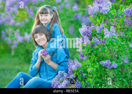 Cute adorable belle mère dame maman femme avec fille brune fille en prairie de lilac bush violet.Les gens en jeans wear Banque D'Images