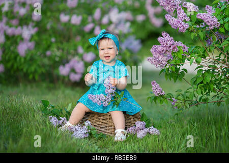 Cute blonde baby girl enjoying time sur un lieu impressionnant entre lilac bush seringue.jeune dame avec panier plein de fleurs vêtue de jeans et élégant s Banque D'Images