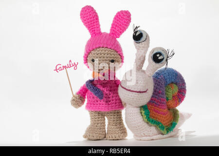 Crochet girl holding sign famille et crochet escargot arc-en-ciel, sur fond blanc. Amigurumi. Handmade Banque D'Images