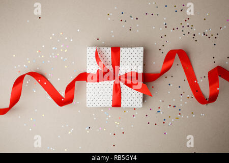 Valentine day composition : boîte-cadeau blanche avec noeud et ruban rouge. confetti, modèle photo, l'arrière-plan. Vue d'en haut. Vue de dessus Banque D'Images