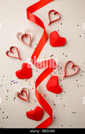 Coeurs en papier rouge et ruban de soie, des confettis sur fond gris. Absctract Saint-valentin. Symbole de l'amour. L'espace de copie, de mise à plat Banque D'Images