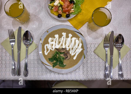 La soupe aux champignons avec de la crème sure et oignon salade de tomates et de pommes de terre rôties, couteau,, sel, poivre, jus et d'autres choses sur la table. Banque D'Images