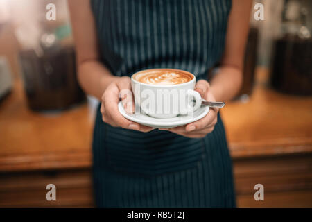 Close up of a waitress holding a coulé bien coffeeCropped Close up de femmes servant du café avec latte art tout en se tenant dans un coffee shop. L'accent sur fe Banque D'Images