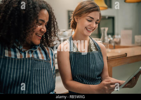 Deux serveurs sourire et rire à quelque chose d'être souligné sur une tablette numérique Banque D'Images