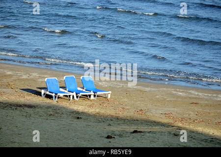 Basse saison. Plage de sable vide avec trois chaises longues en plastique blanc sur le sable près de l'avant-garde seacoast mer avec de petites vagues sur la journée ensoleillée Banque D'Images