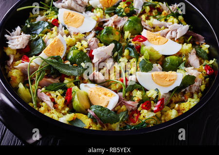 Close-up of delicious avec Kedgeree en flocons poissons fumés, œufs durs, du riz, chou frisé, chou de Bruxelles, les épices et les herbes dans une cocotte noire sur une woo Banque D'Images