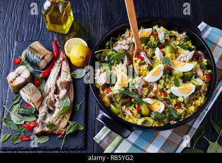 Kedgeree délicieux avec le poisson fumé émietté, œufs durs, du riz, chou frisé, chou de Bruxelles, les épices et les herbes dans une cocotte sur une table en bois noir wi Banque D'Images