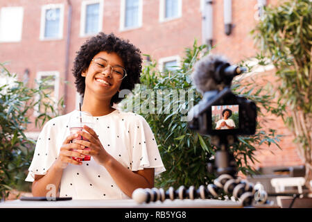 Happy woman l'enregistrement d'une vidéo sur votre appareil photo reflex numérique, un jus holding Banque D'Images