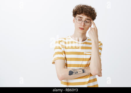 Guy nerdy puzzle résoudre dans l'esprit, sérieux et déterminé sur la tête avec le matériel roulant curl à doigt dans le coin inférieur gauche ciblées que la pensée, réfléchie et qui inquiète de mur gris Banque D'Images