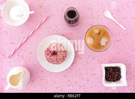 Dépoli rose donut coloré avec sprinkles, un verre rempli de préparer de café froid, froid préparer du café se concentrer dans une petite bouteille de lait et une paille sur p Banque D'Images