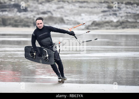 Un kite surfer se penche vers le vent comme il se débat avec son cerf-volant alors qu'il se prépare à entrer dans la mer au repos, la baie de Porthcawl, dans des conditions de vent sur la côte sud du Pays de Galles. Banque D'Images